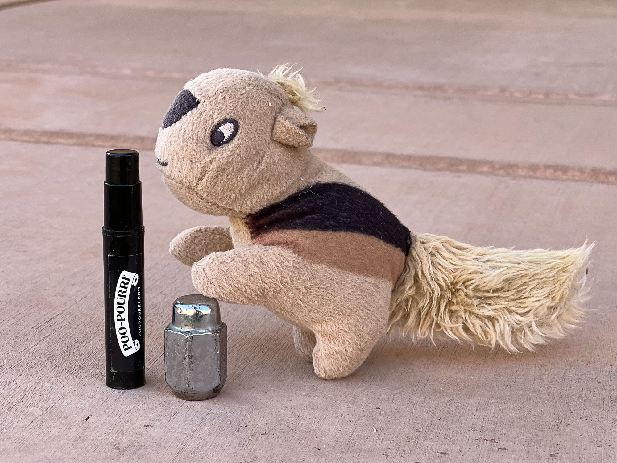 Stuffed chipmunk doll poised on a chrome wheel lug nut smelling the Poo Pourie (odor eliminator) bottle.