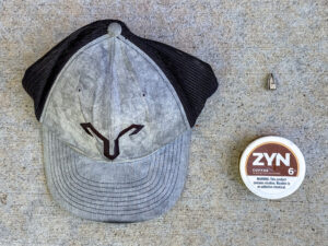 Gray trucker cap, chrome presta valve cap, ZYN coffee-flavored nicotine pouch container