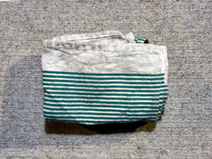 A folded, slightly dirty white kitchen towel with thin green stripes