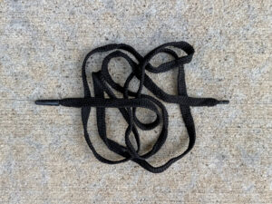 Single black shoelace with plastic tips, loosely coiled