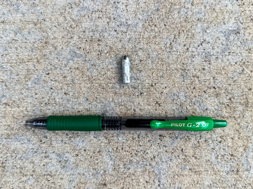 Bullet-shaped steel rivet drive pin and a Pilot G2 green pen