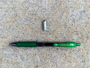 Bullet-shaped steel rivet drive pin and a Pilot G2 green pen