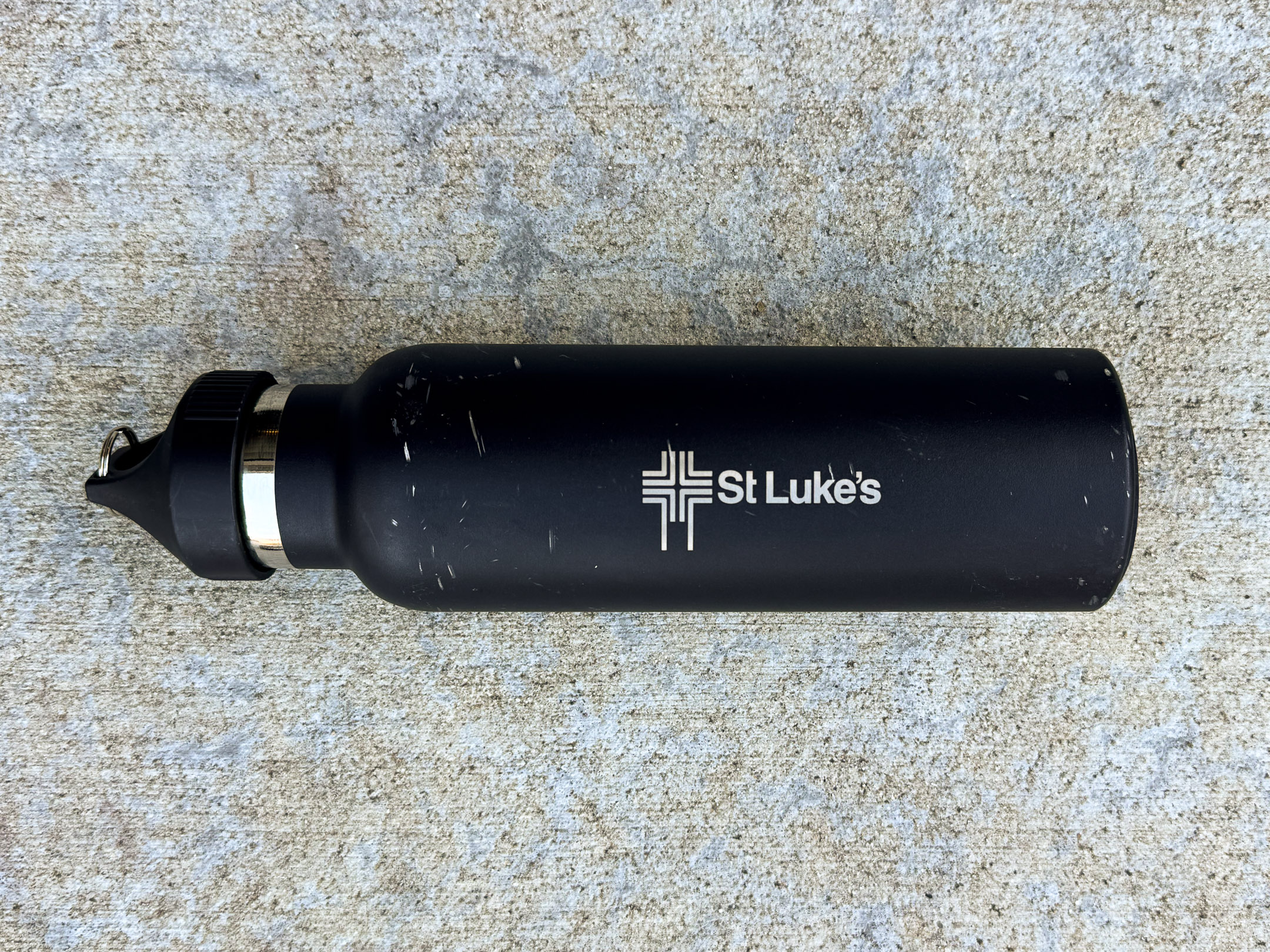 Black metal TOPL water bottle with silver "St Luke's" logo, showing light wear and scratches