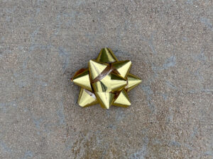 Shiny gold gift bow on a wet concrete surface.