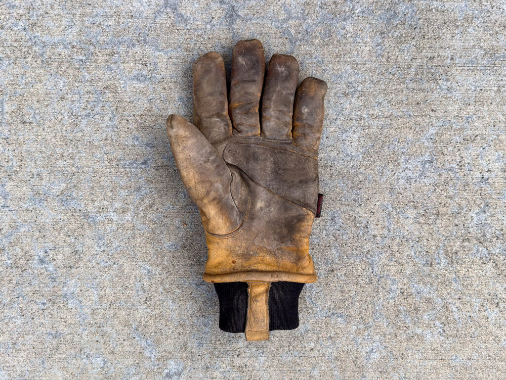A dirty and worn left-hand leather work glove.