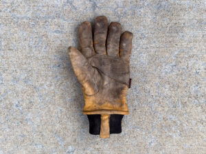 A dirty and worn left-hand leather work glove.