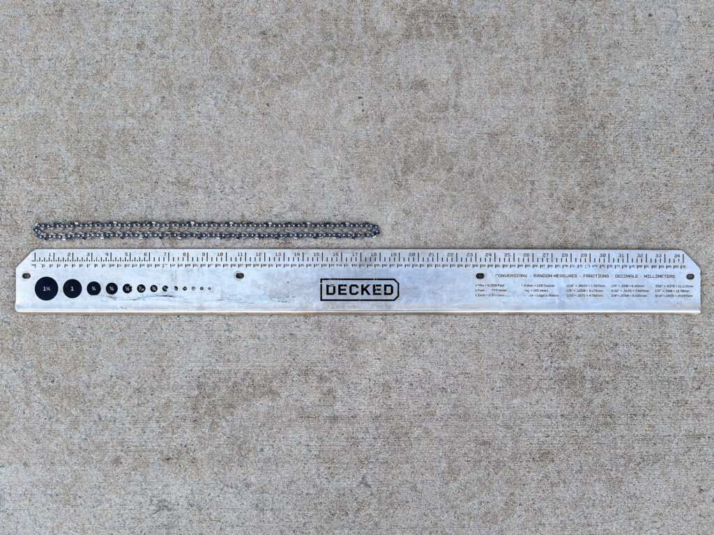 A metal ruler for the DECKED truck storage system displayed below an 18-inch chainsaw chain arranged in a narrow loop.