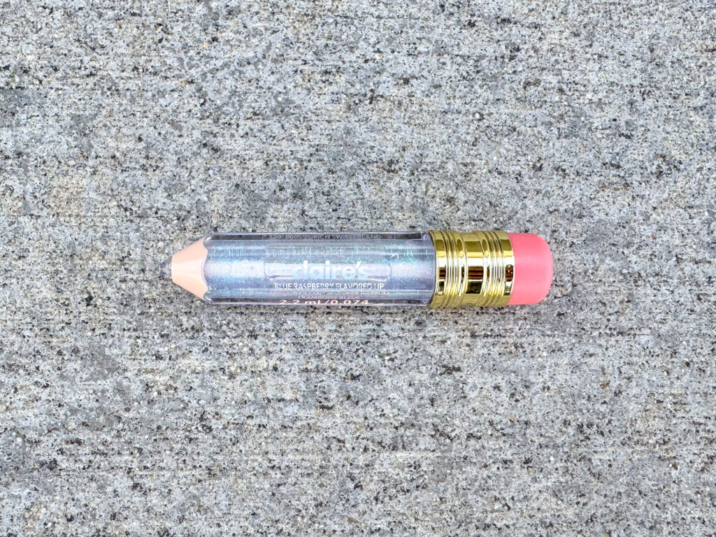 Claire's Shimmer Pencil Lip Gloss (blue raspberry flavor), designed to look like a short, glittery pencil with a gold ferrule and a pink eraser cap.