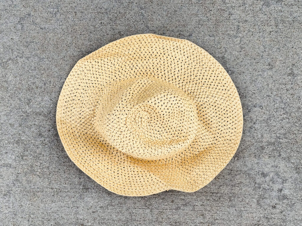 A slightly crumpled woven straw sun hat with a wide brim and an open-weave pattern.