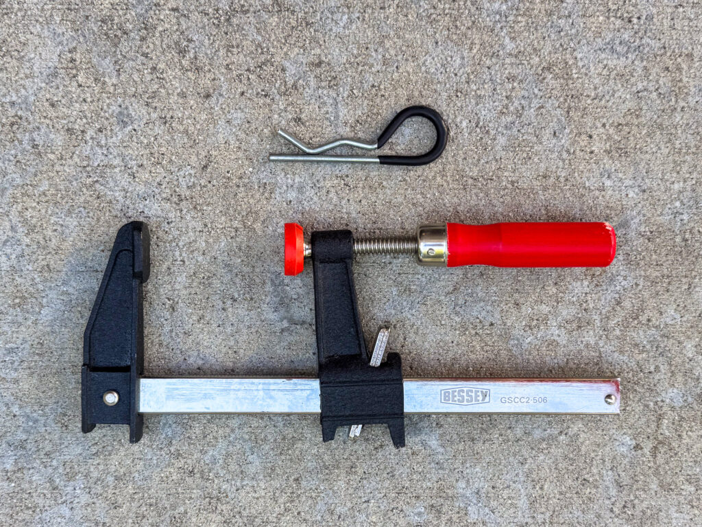 A trailer hitch pin clip with a black vinyl grip and a Bessey GSCC2-506 bar clamp with a red handle.