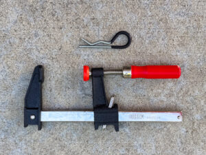 A trailer hitch pin clip with a black vinyl grip and a Bessey GSCC2-506 bar clamp with a red handle.