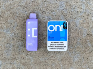 Purple Mi-Pod Rocket Popsicle vape pod next to a blue and white on! Mint 4mg nicotine tin with a message that reads, "WARNING: This product contains nicotine. Nicotine is an addictive chemical."