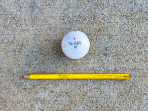 Scuffed Top-Flite XLII golf ball with the number 4, next to a weathered yellow Crayola pencil with a splitting end.