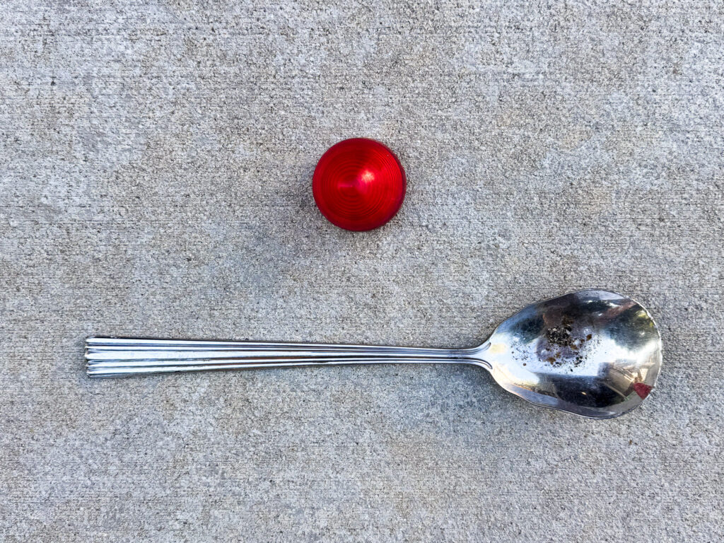A 2-inch red beehive trailer light positioned above a large silver serving spoon with a pitted bowl.