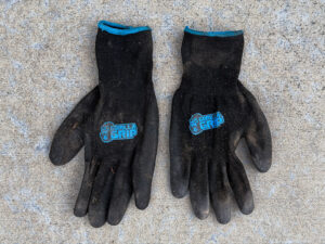 Dirty black work gloves with blue cuffs. Each glove shows a blue gorilla head and "GORILLA GRIP" text on the back.