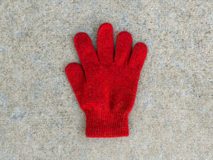 Small red knit glove with five fingers, laid flat with the cuff at the bottom. The fabric has fine glittery flecks woven throughout.