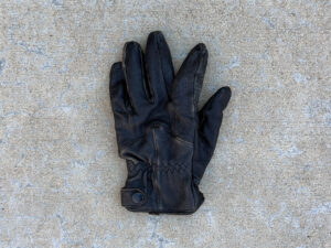 Black leather left glove with a snap strap at the wrist, laid flat.
