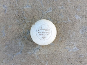 Lightly scuffed white lacrosse ball with printed text “Champion Sports NOCSAE® SEI NFHS NCAA”.
