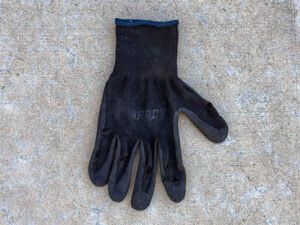 Black, soiled Hardy work glove with visible wear and holes on each finger and the thumb.