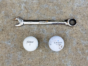 Husky ratcheting combination wrench labeled 14 mm on both ends with visible rust spots, placed above two golf balls—one Titleist 1 and one Top Flite—both showing light scuffs.