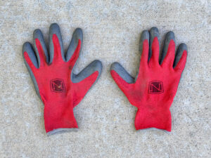 Pair of red work gloves with gray rubber-coated palms and fingers, showing light dirt and wear, laid flat side by side.