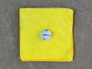 White Wilson golf ball with green markings and scuffed lettering resting on a folded yellow microfiber towel.