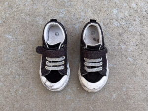Pair of worn sparkly black toddler sneakers with gray elastic laces, hook-and-loop straps, dirty white rubber toes, and size 7 markings inside both shoes.