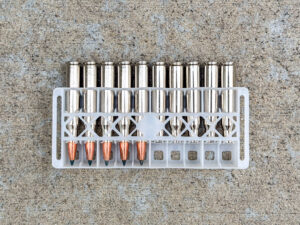 Plastic ammunition tray holding ten shiny silver rifle cartridge cases: five loaded rounds with copper-colored pointed bullets and five spent casings.