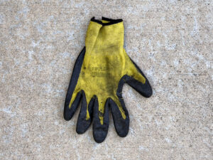 Dirty yellow-and-black Firm Grip work glove with black coated fingers and palm, worn fabric, and faded markings on the back.
