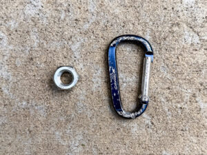 Silver hex nut beside a scuffed blue and silver aluminum Colonial Life carabiner with a silver spring gate, likely a promotional swag item.